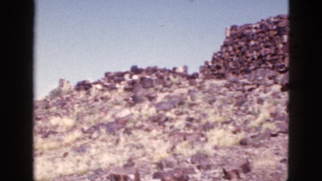Rocky slope with dry grass and a taller stacked stone wall at the upper right.