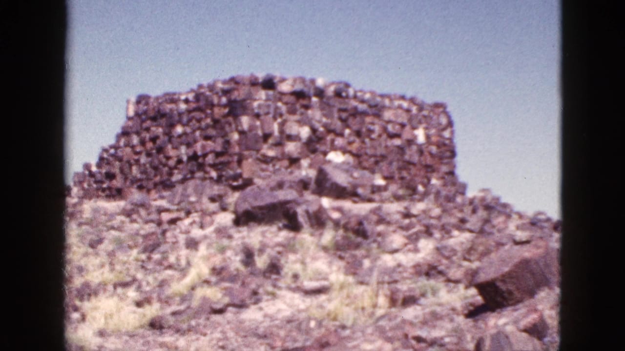 1953 Arizona 8mm frame showing a weathered stone wall or ruin on a rocky desert slope with sparse vegetation.