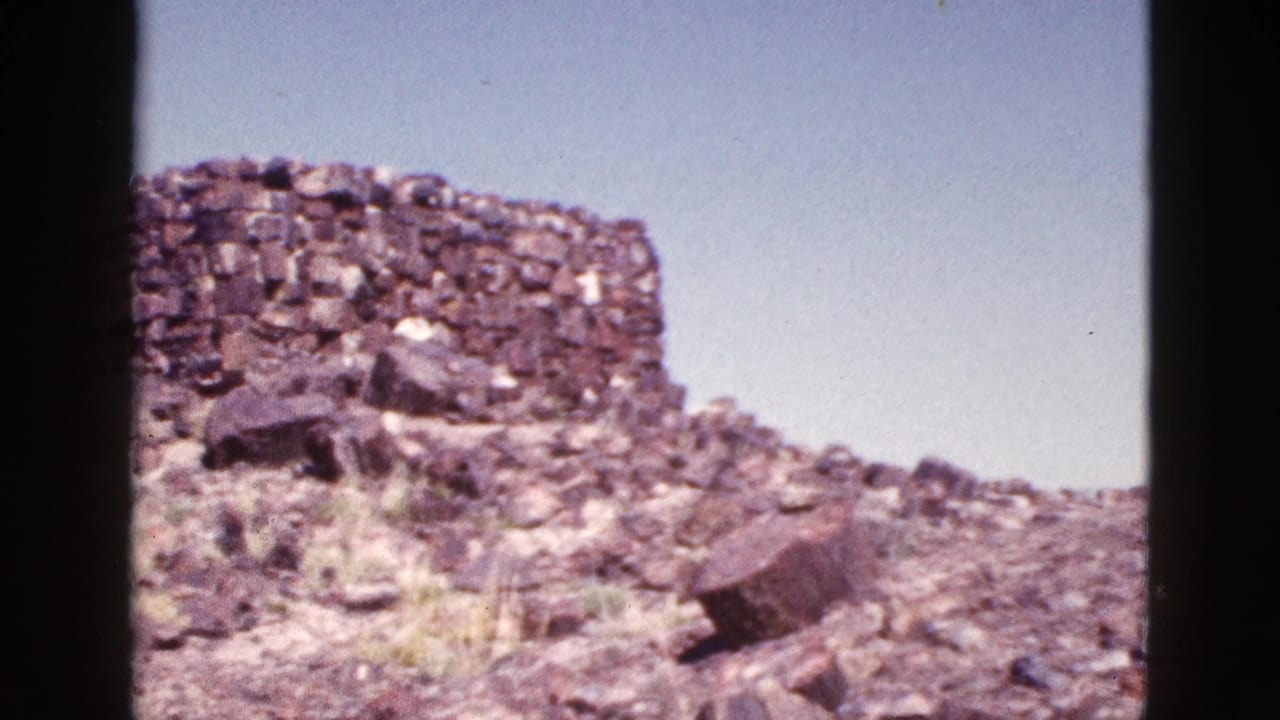 Stone ruin on a rocky slope with open sky and desert ground.