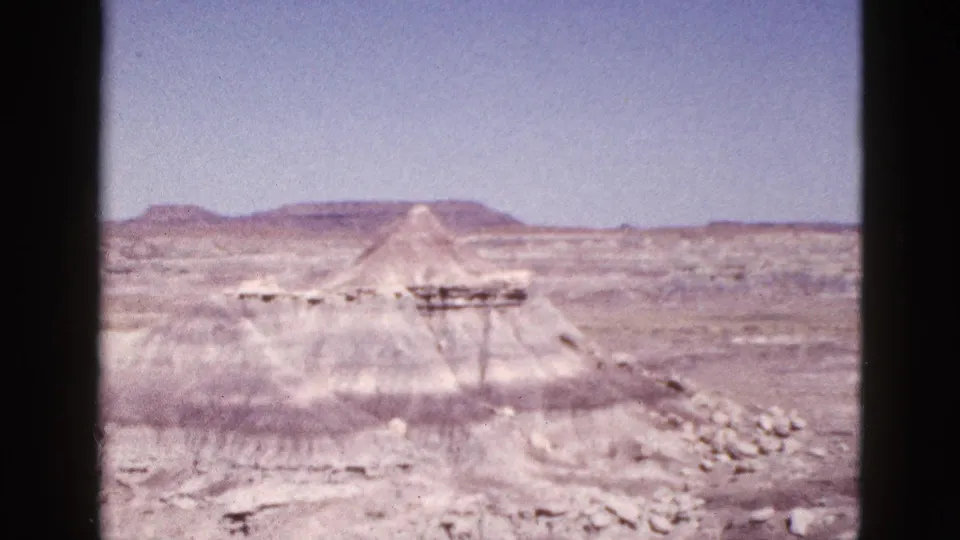 1953 Arizona 8mm frame showing a pale pyramid-like mound or structure in desert terrain with mesas on the horizon.