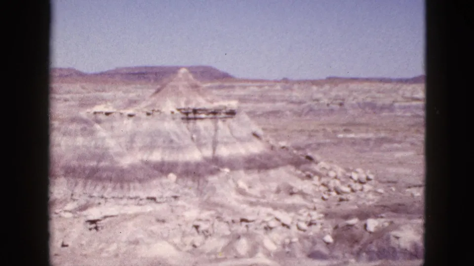 1953 Arizona 8mm view across a rocky desert site toward a pyramid-like structure and low mesas beyond.