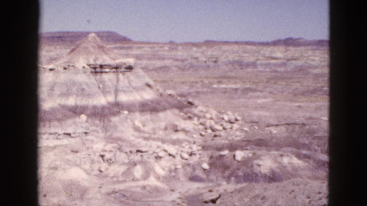 Wide desert canyon view with pale rock mounds and distant ridges.