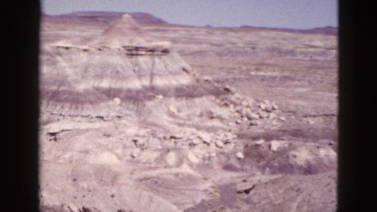 1953 Arizona 8mm frame showing pale layered desert rock and distant mesas under a washed sky.