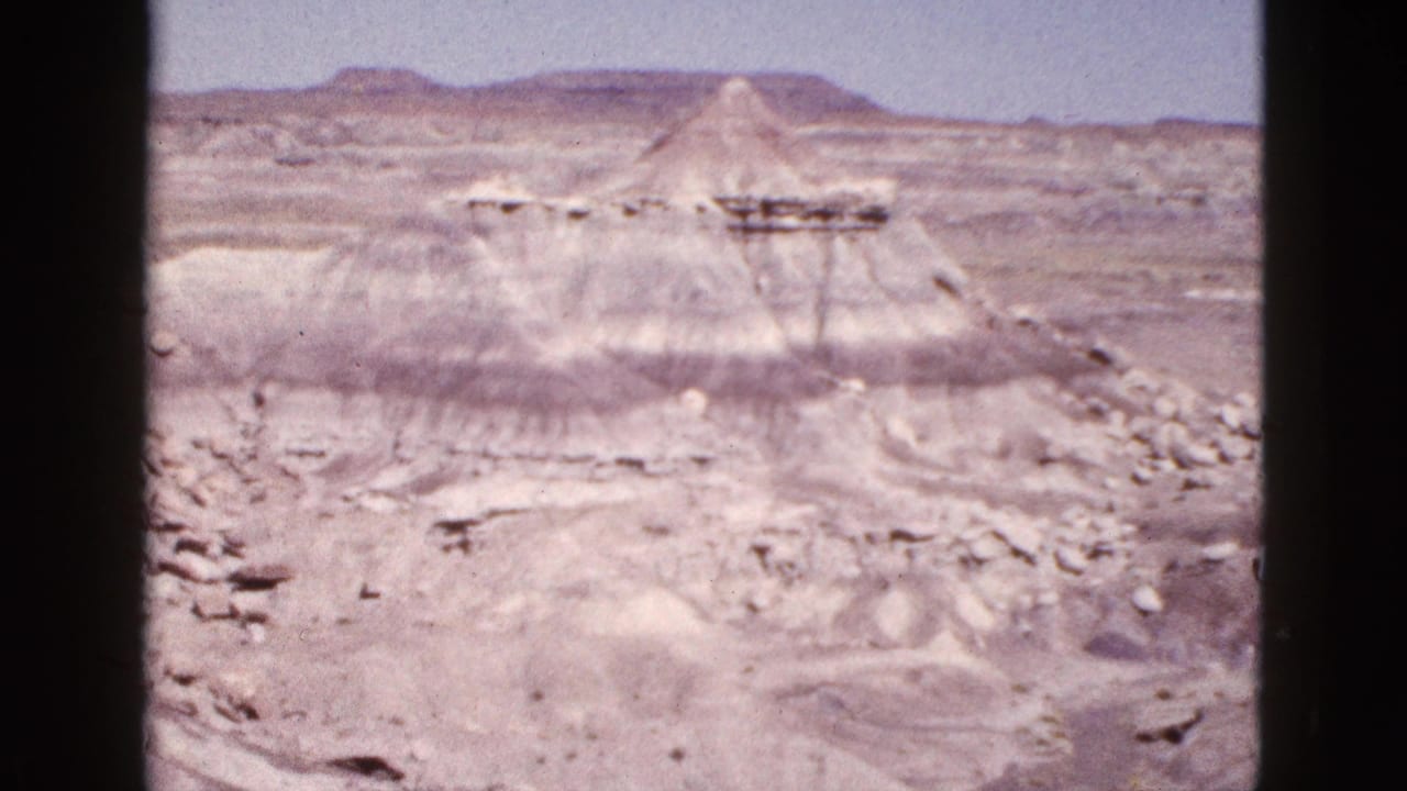Desert ridge with a conical butte and horizontal rock layers in the distance.