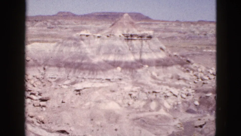 1953 Arizona desert view with a conical butte, pale ridges, and layered rock bands in soft 8mm color.