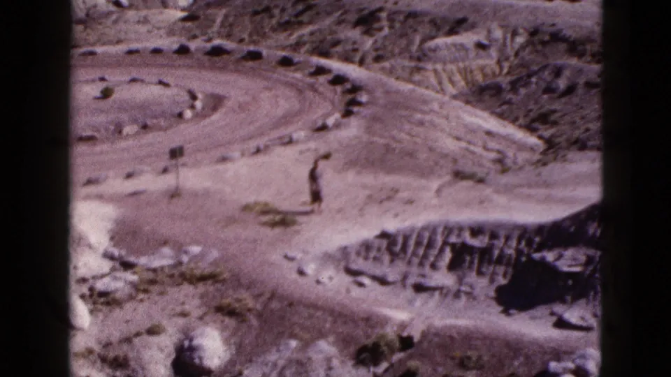 1953 Arizona desert frame showing a winding dirt path through eroded terrain, with a tiny lone figure possibly visible near the path.