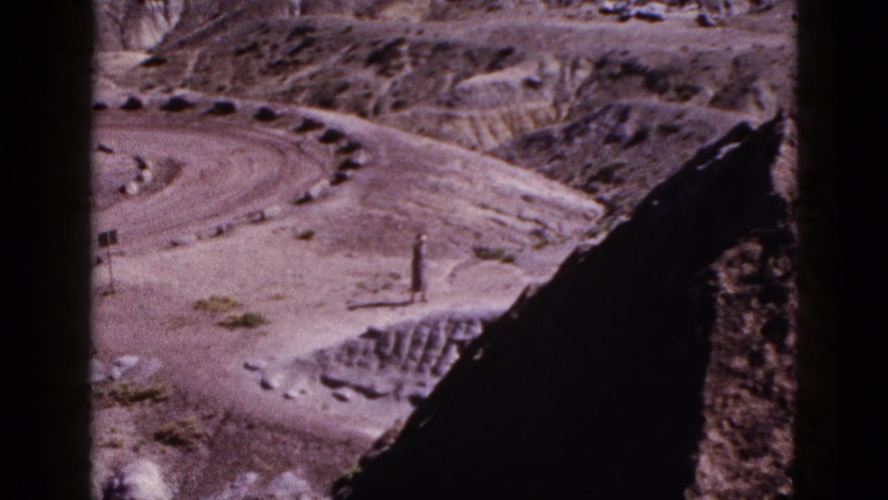 1953 Arizona 8mm frame showing a lone man small in scale among dry hills, rocks, and a curving dirt road.