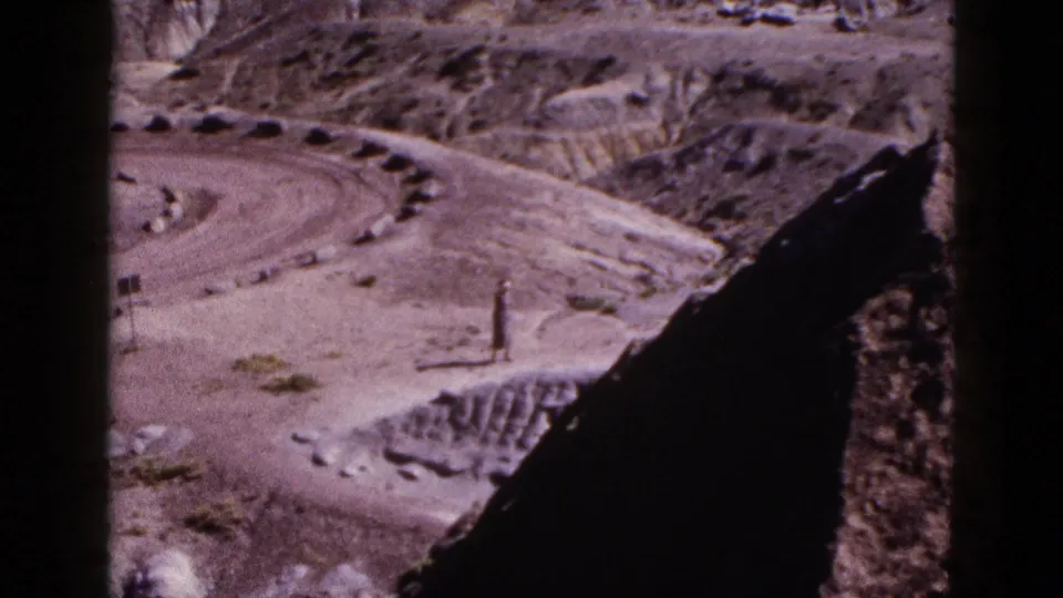 1953 Arizona 8mm frame showing a lone man small in scale among dry hills, rocks, and a curving dirt road.