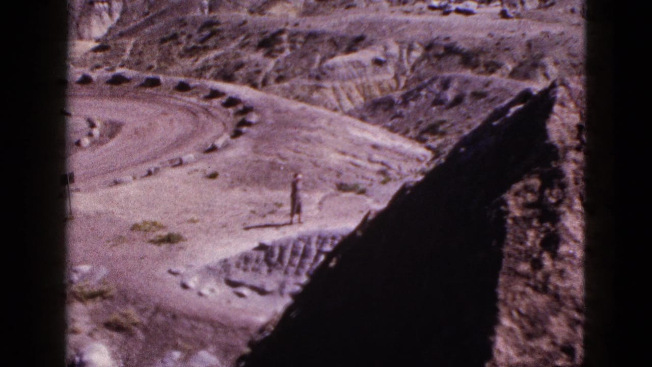 Distant man in dry hills seen through dark vertical film or window edges.