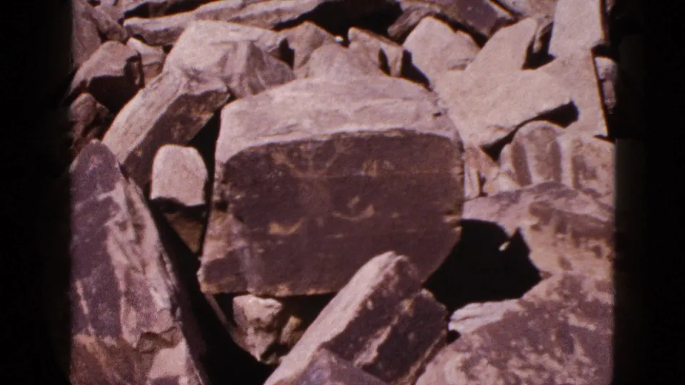 Close 8mm frame from the Arizona landscape footage showing rough stones and broken rock slabs in sunlit dry terrain.