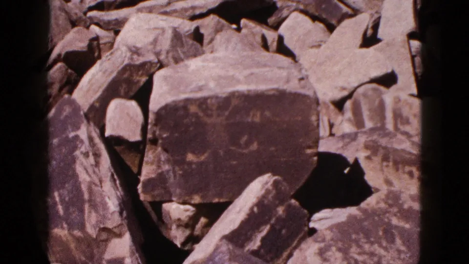 1953 Arizona 8mm frame with the petroglyph boulder centered among irregular sunlit stones and dark crevices.