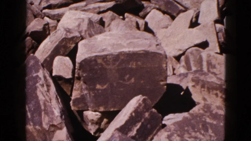 1953 Arizona 8mm frame holding on a dark marked boulder within a pile of weathered desert rocks.