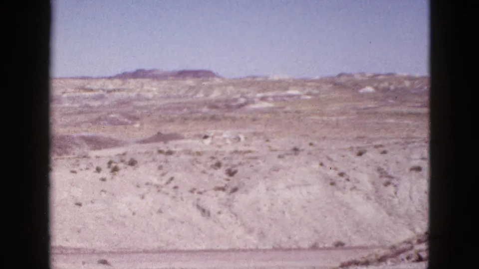 Wide 1953 Arizona 8mm landscape showing open arid terrain, distant low hills, pale washes, and sparse desert vegetation.