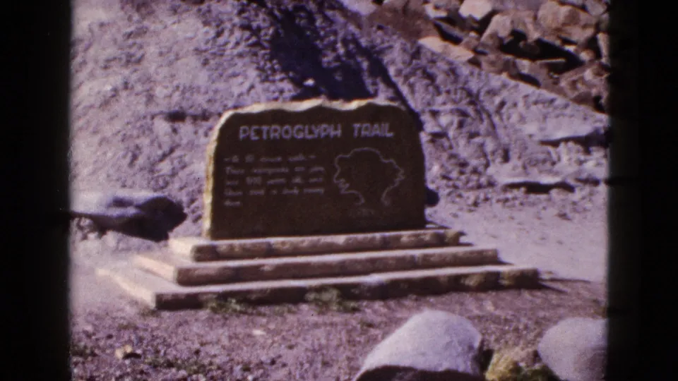 1953 Arizona home-movie still of the Petroglyph Trail marker, softened by grain and film-gate edges.