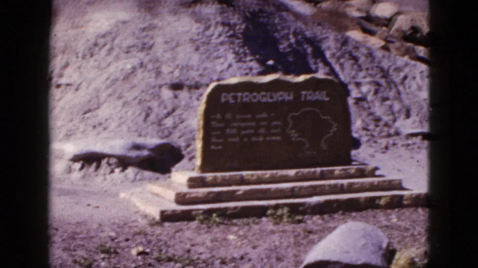 1953 Arizona 8mm still with the Petroglyph Trail sign centered against a rocky desert slope.
