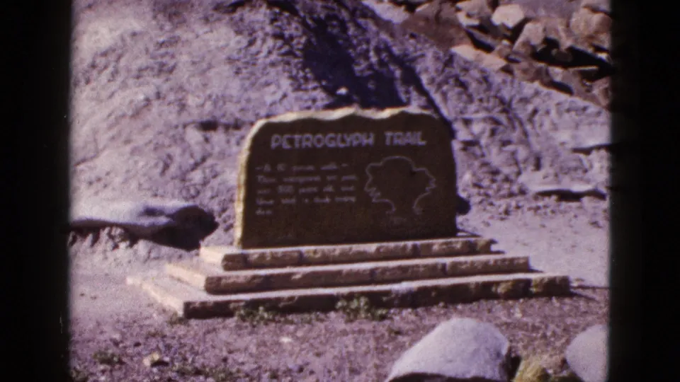Final 1953 Arizona frame of a Petroglyph Trail marker, with boulders and hillside visible around the sign.