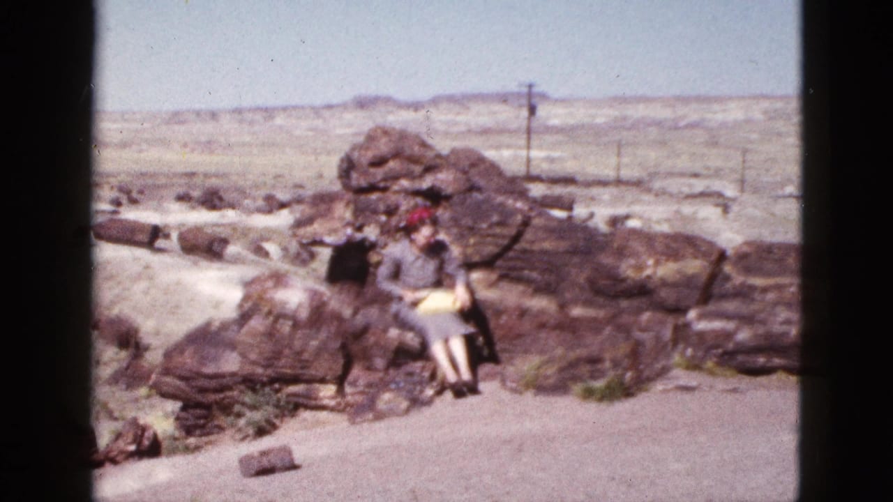 1953 Arizona home-movie frame of a woman seated on a rock formation in an open desert landscape, holding a yellow object.