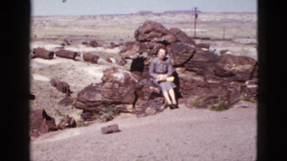 Mid-century Arizona travel frame with a woman sitting on layered rocks against a wide desert horizon.