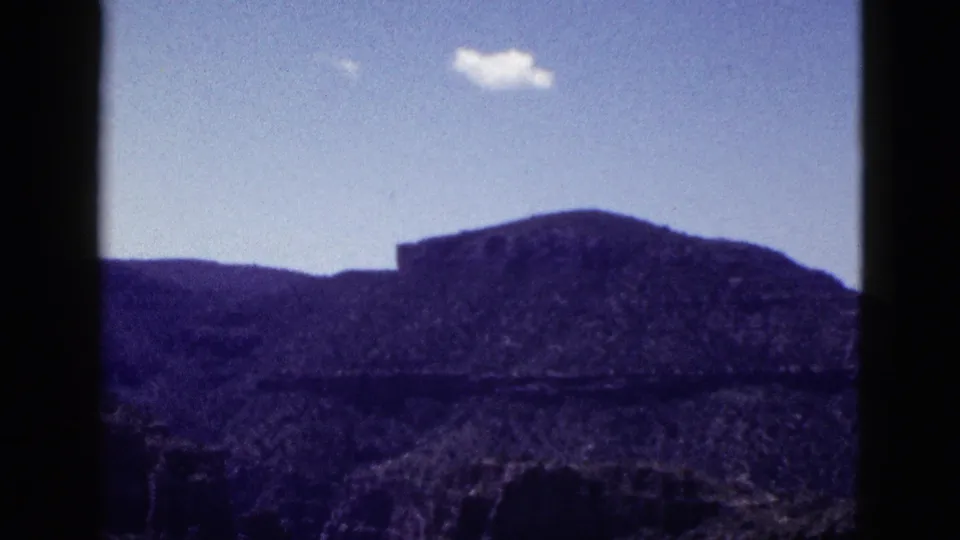 1953 Arizona home-movie frame showing a distant rocky mesa or mountain under blue sky, with no people visible in this still.