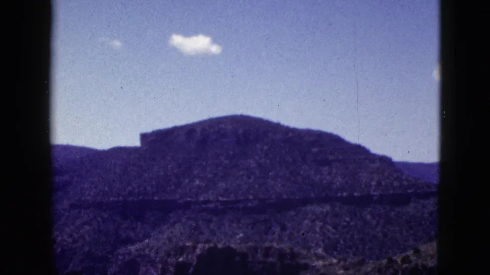 1953 Arizona landscape frame with a distant mesa, rough desert terrain, and a single small cloud in the blue sky.