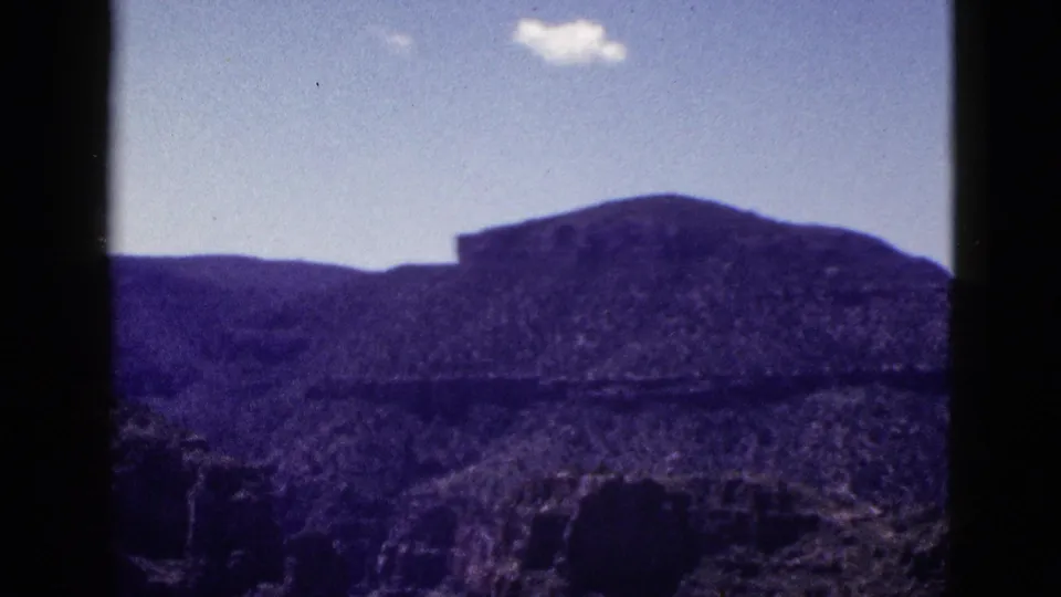 1953 Arizona home-movie frame showing a broad rocky desert view with a dark mesa and clear blue sky.