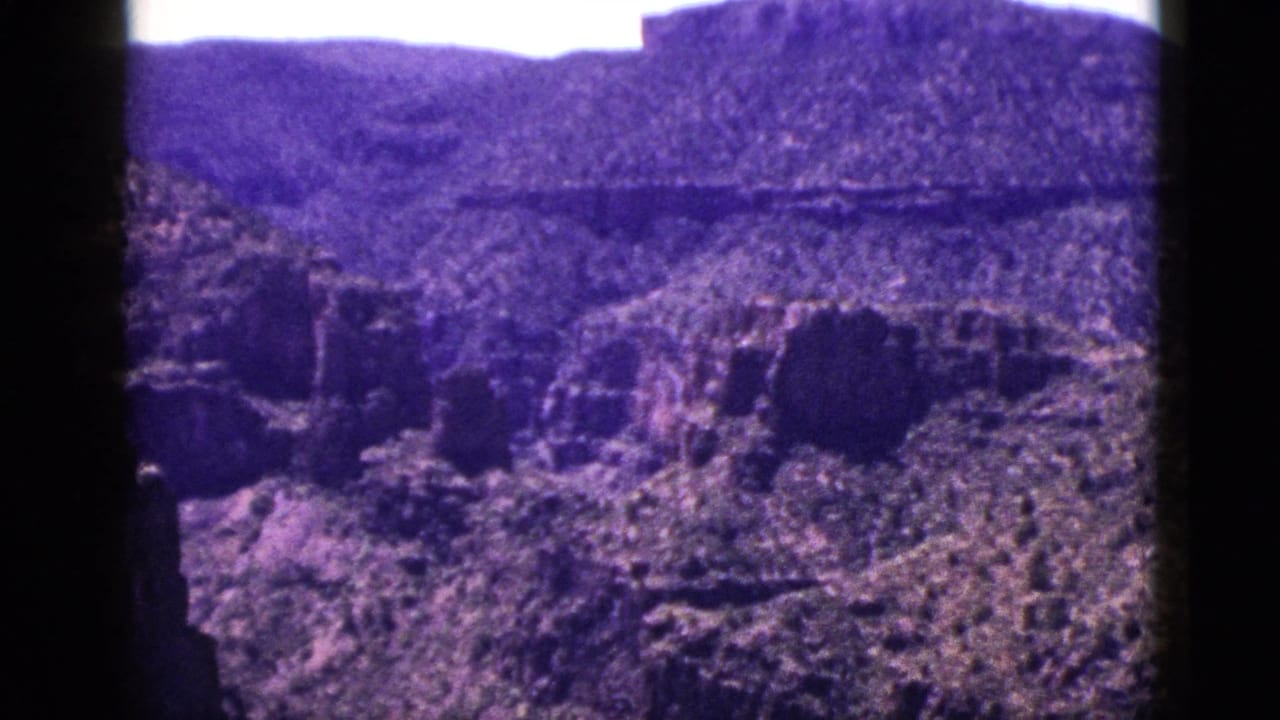 1953 New Mexico 8mm view of a rocky canyon with steep formations, sparse vegetation, distant plateau, and visible gate-edge shadows.