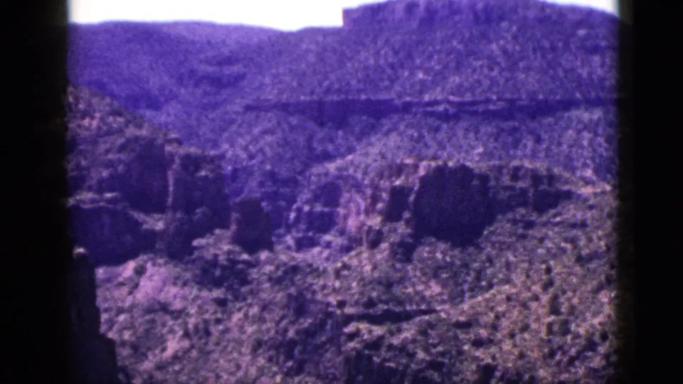 1953 New Mexico 8mm view of a rocky canyon with steep formations, sparse vegetation, distant plateau, and visible gate-edge shadows.