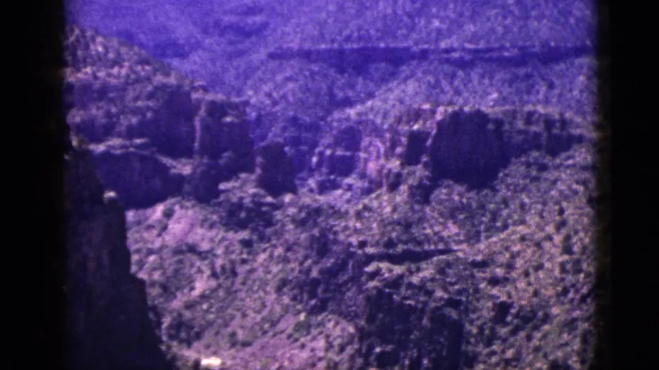 1953 New Mexico 8mm frame showing rough canyon slopes, layered cliffs, sparse brush, and a dark foreground film edge during the pan.