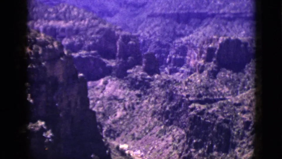 1953 New Mexico 8mm view across rugged canyon formations, arid brush, layered rock, and distant high ground under a pale sky.