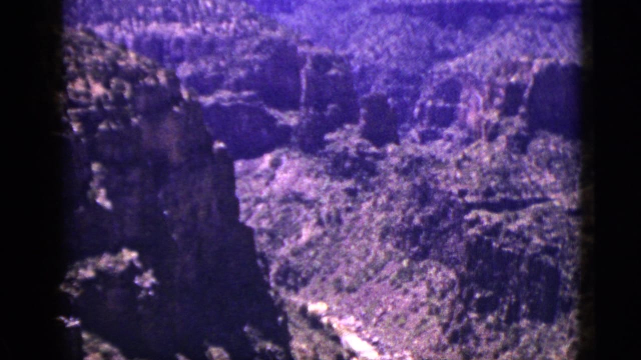 Purple-shifted 8mm view of a steep canyon with a pale stream below.