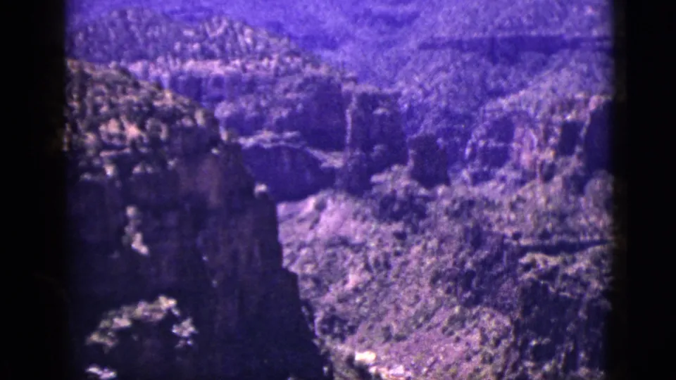 1953 New Mexico home-movie frame of a rugged canyon, dark rock shadows, and a bright runoff channel below.
