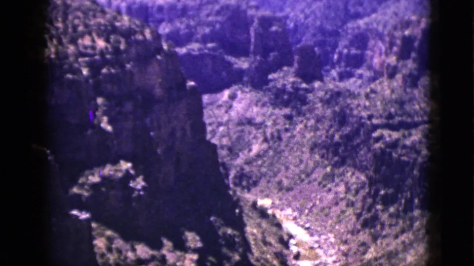 Color-shifted 1953 New Mexico 8mm frame showing steep canyon formations and melting snow runoff along the valley floor.
