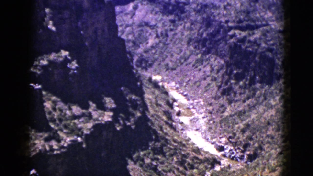 High view into a rocky canyon with a bright winding river and dark forested slopes.
