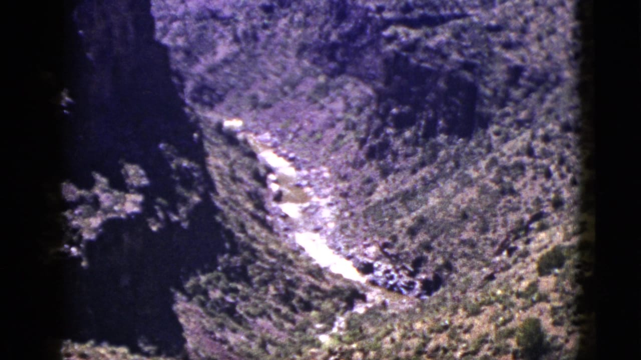 Rocky canyon landscape with a pale river line running between steep wooded slopes.