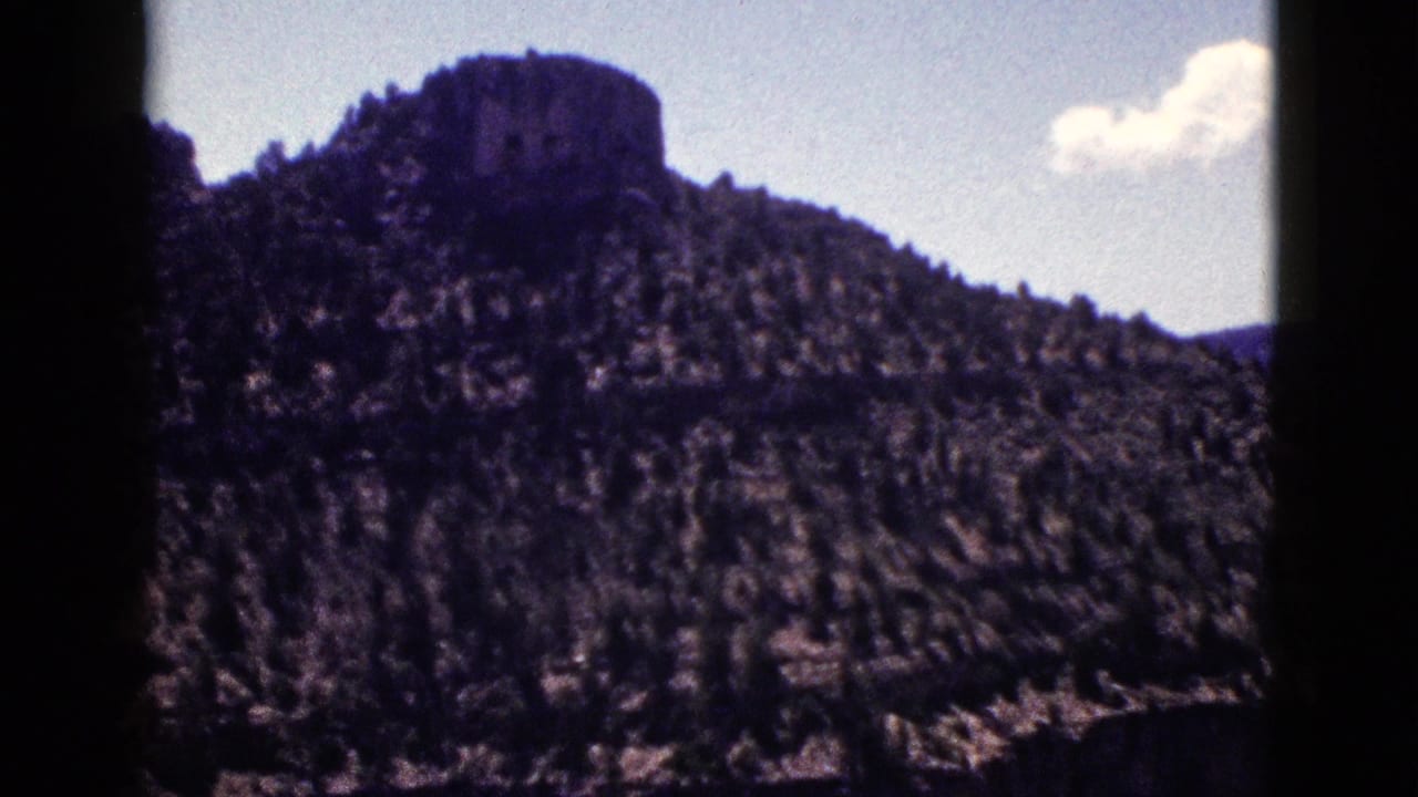 1953 New Mexico 8mm frame showing a forested ridge and distinctive rocky summit beneath a small cloud.