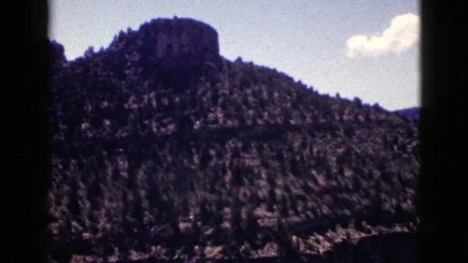 1953 New Mexico 8mm frame showing a forested ridge and distinctive rocky summit beneath a small cloud.
