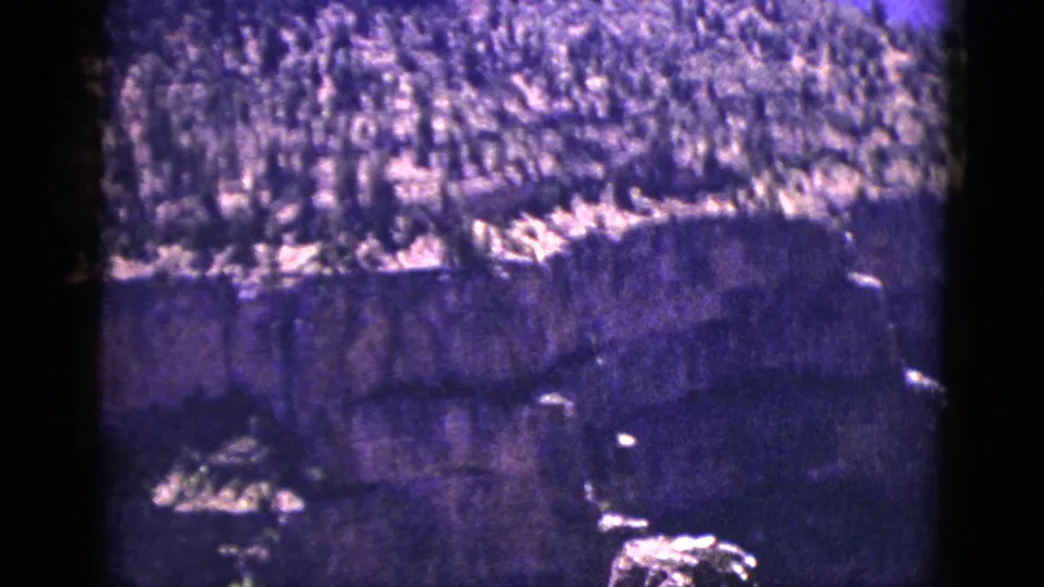 Faded 8mm frame from New Mexico showing a steep, layered cliff beneath a brush-covered hillside.