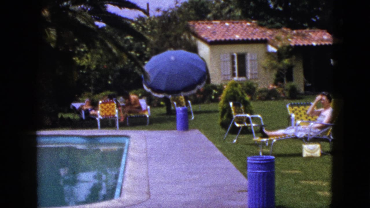 Poolside lawn scene with adults seated near a blue umbrella and a woman reclining at right.