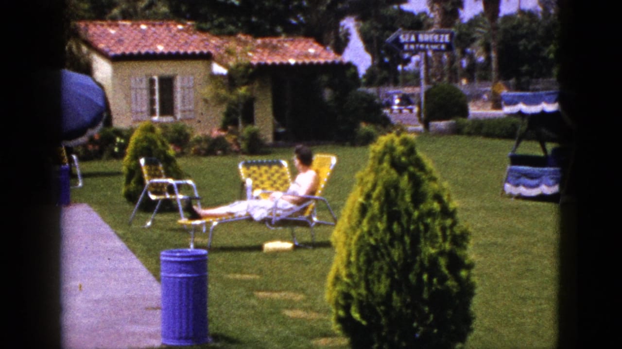 Woman reclining on a yellow lounge chair on a motel lawn near a stucco building.