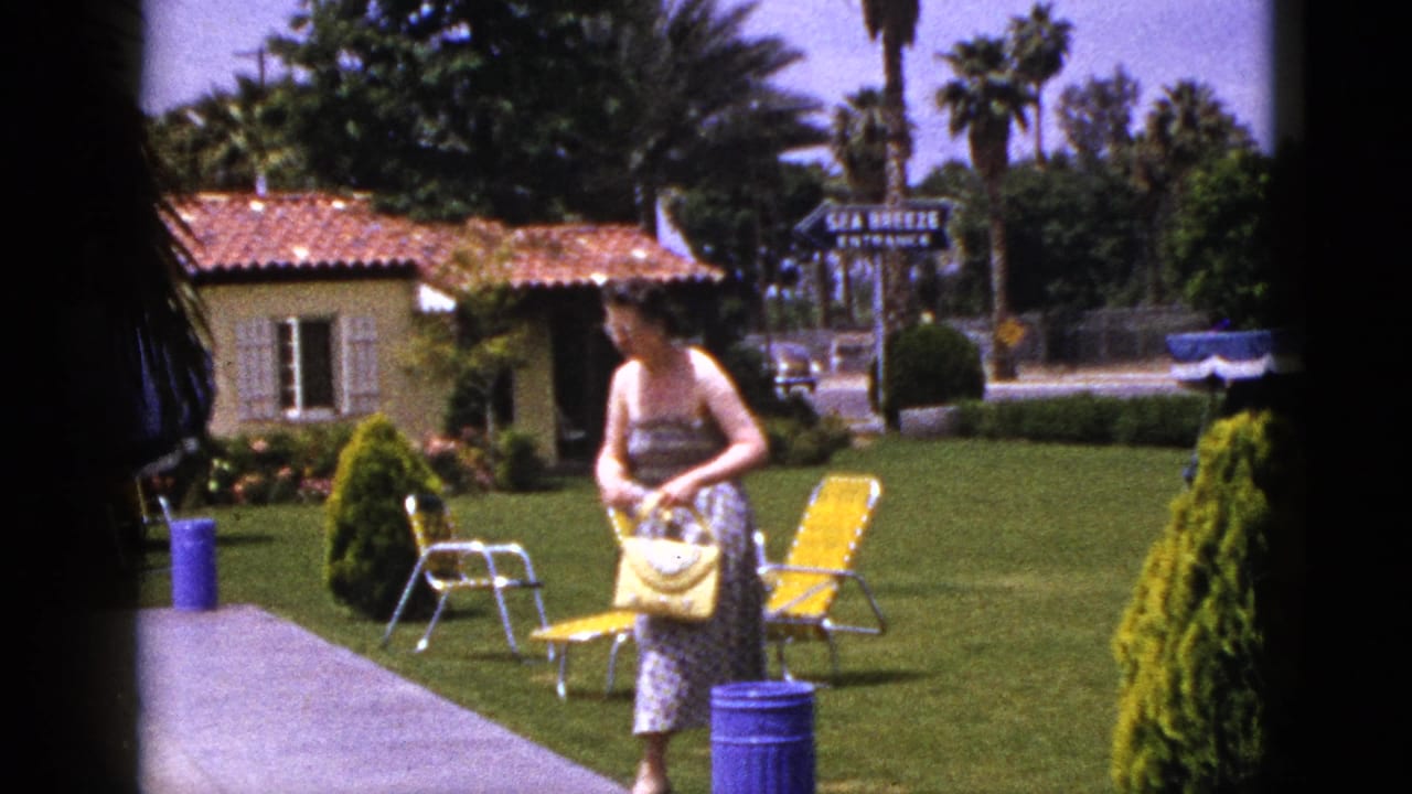 Woman walking beside yellow chairs and a blue trash can on a motel lawn.