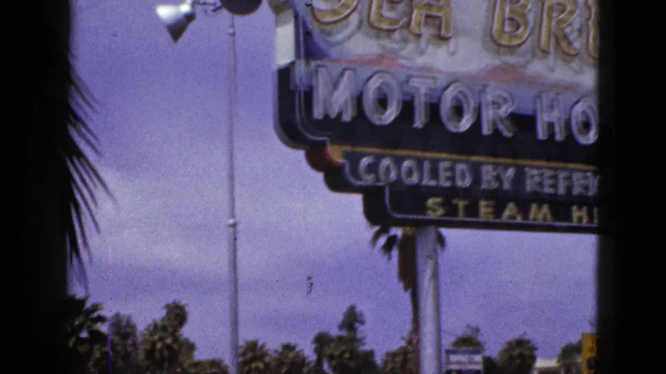 1953 New Mexico home-movie frame with a close view of a Sea Breeze Motor Hotel sign, sky, and palms.