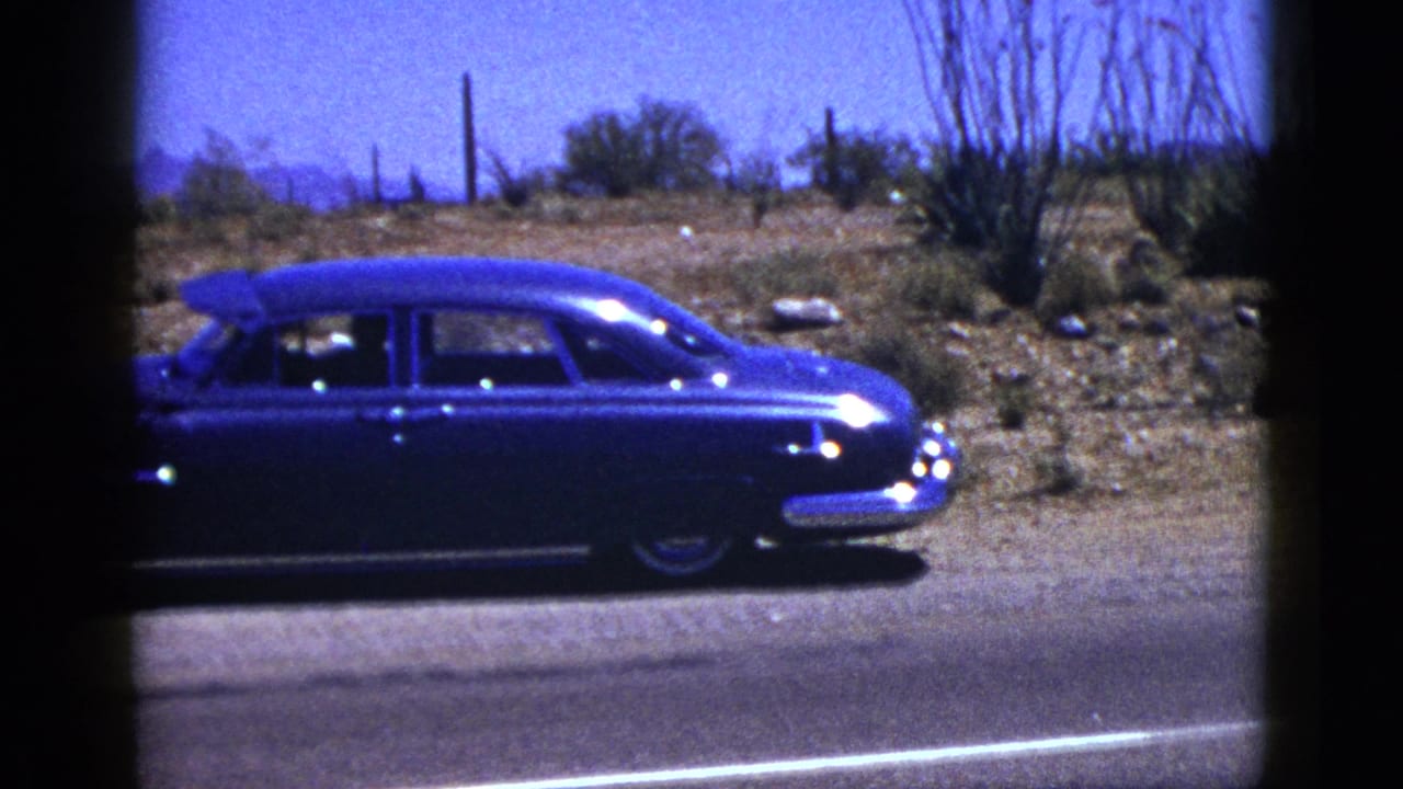 Blue sedan seen from the side on a paved road with desert plants behind it.