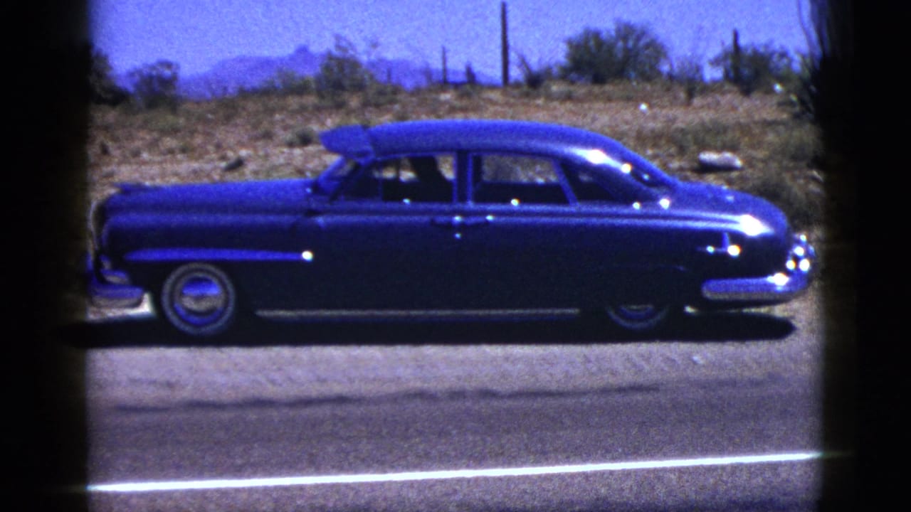 Blue sedan centered on a desert road, framed by dark film borders.