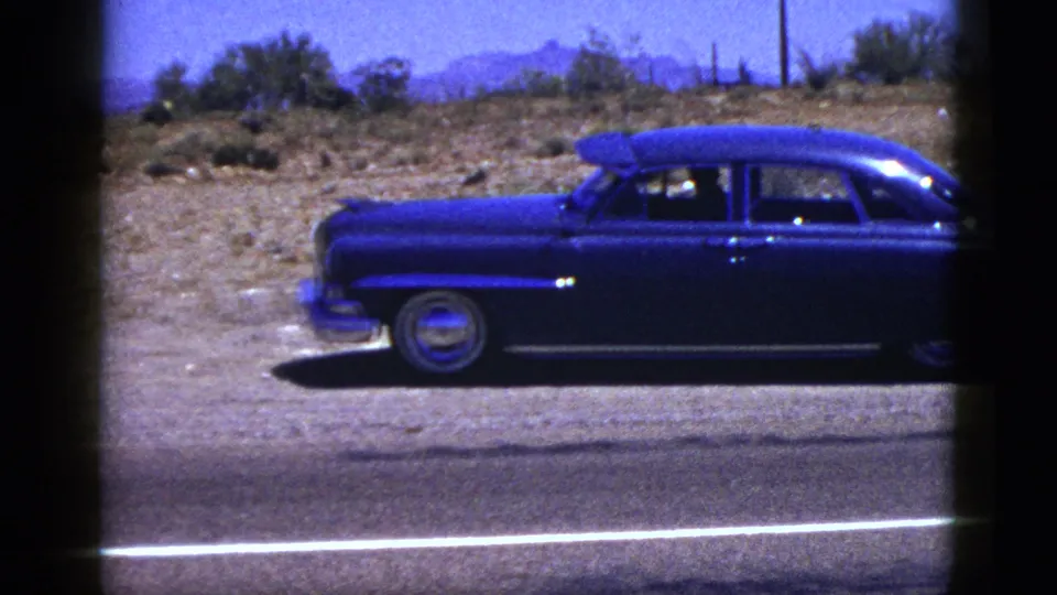 Palm Desert road footage shows the blue sedan partly cropped while passing scrubland and a visible road stripe.
