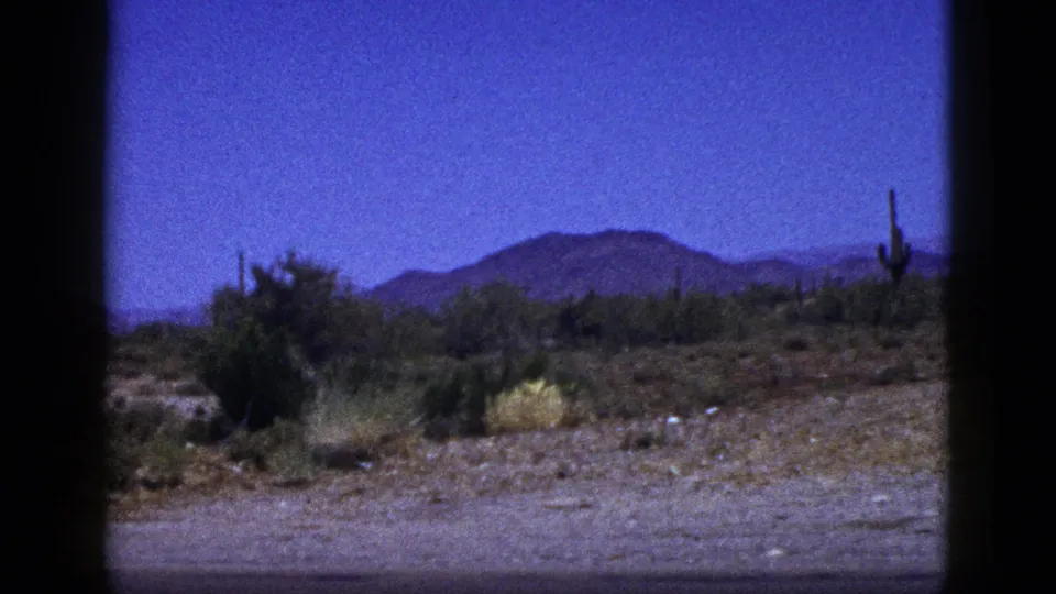 Final 1953 Palm Desert frame showing scrubby desert foreground, cactus silhouettes, and a mountain backdrop in 8mm color.