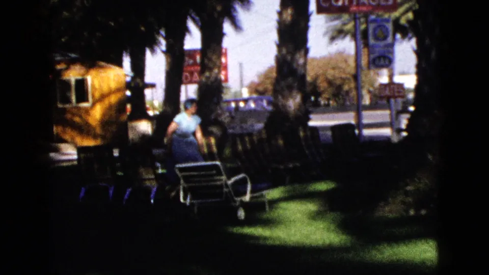 A woman walks through the shaded Desert Palms Guest Cottages lawn near rows of chairs and palm trees.