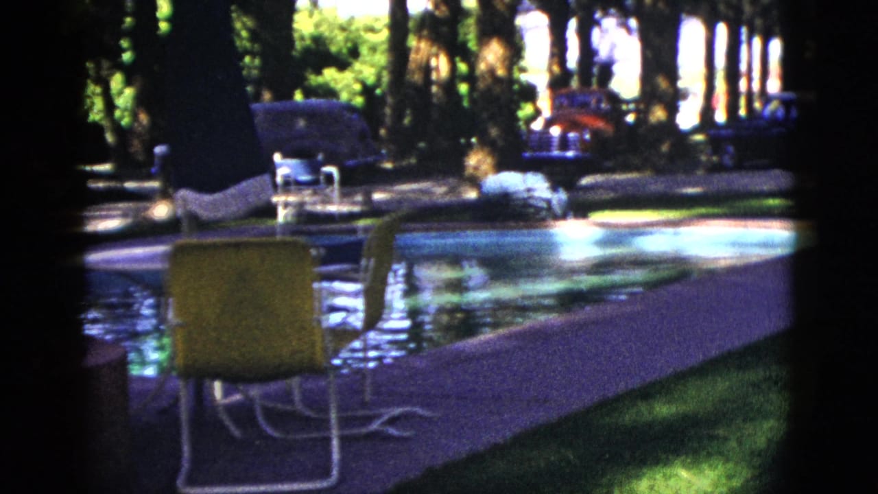 Poolside chair beside reflective water with palms, trees, and cars beyond the deck.