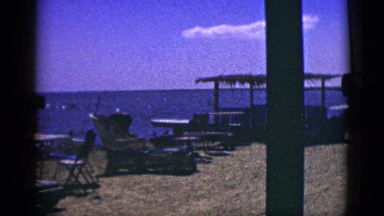 Outdoor seating and lounge chairs near water under a bright sky.