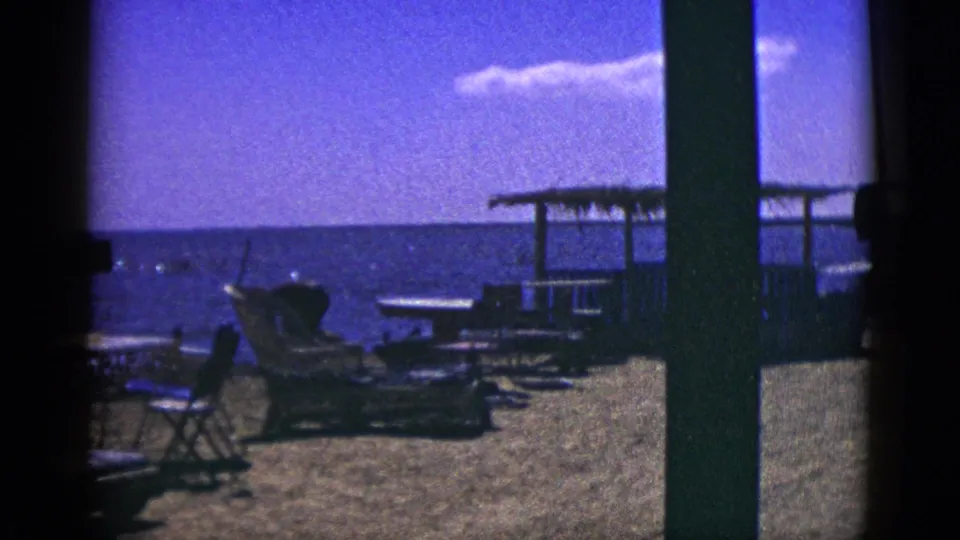 Palm Desert home-movie frame with lounge seating, a shaded structure, bright sky, and a distant water or horizon view.