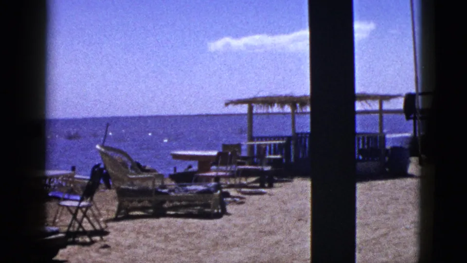 1953 Palm Desert frame showing lounge chairs and small patio furniture silhouetted against a bright water or sky horizon.